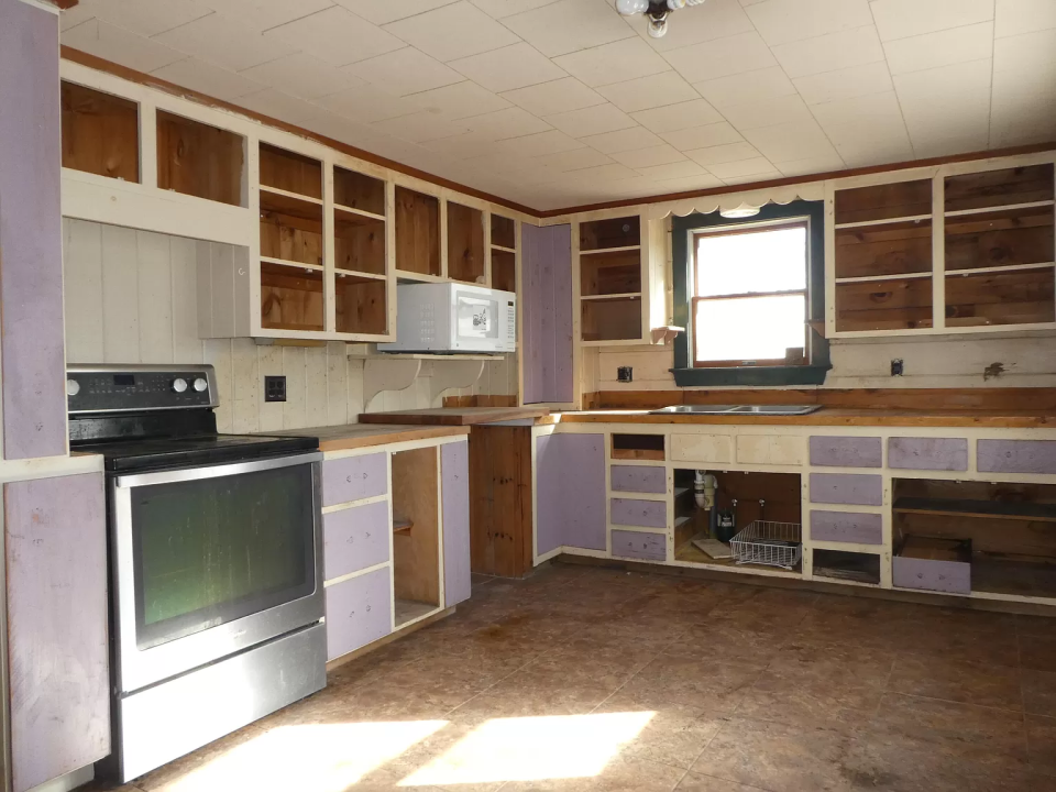 Empty kitchen with wood cabinets, purple trim, stainless steel stove, microwave, and brown floor.