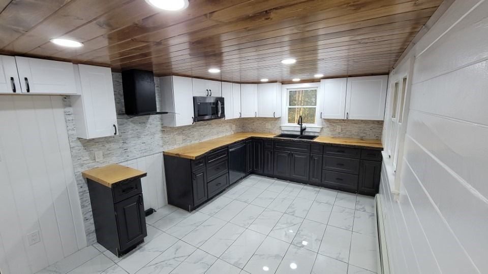 L-shaped kitchen with white upper cabinets and black lower cabinets, wood countertops, and wood ceiling.