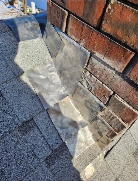Close-up of a brick chimney flashing, with gray roofing shingles and shiny metal flashing.