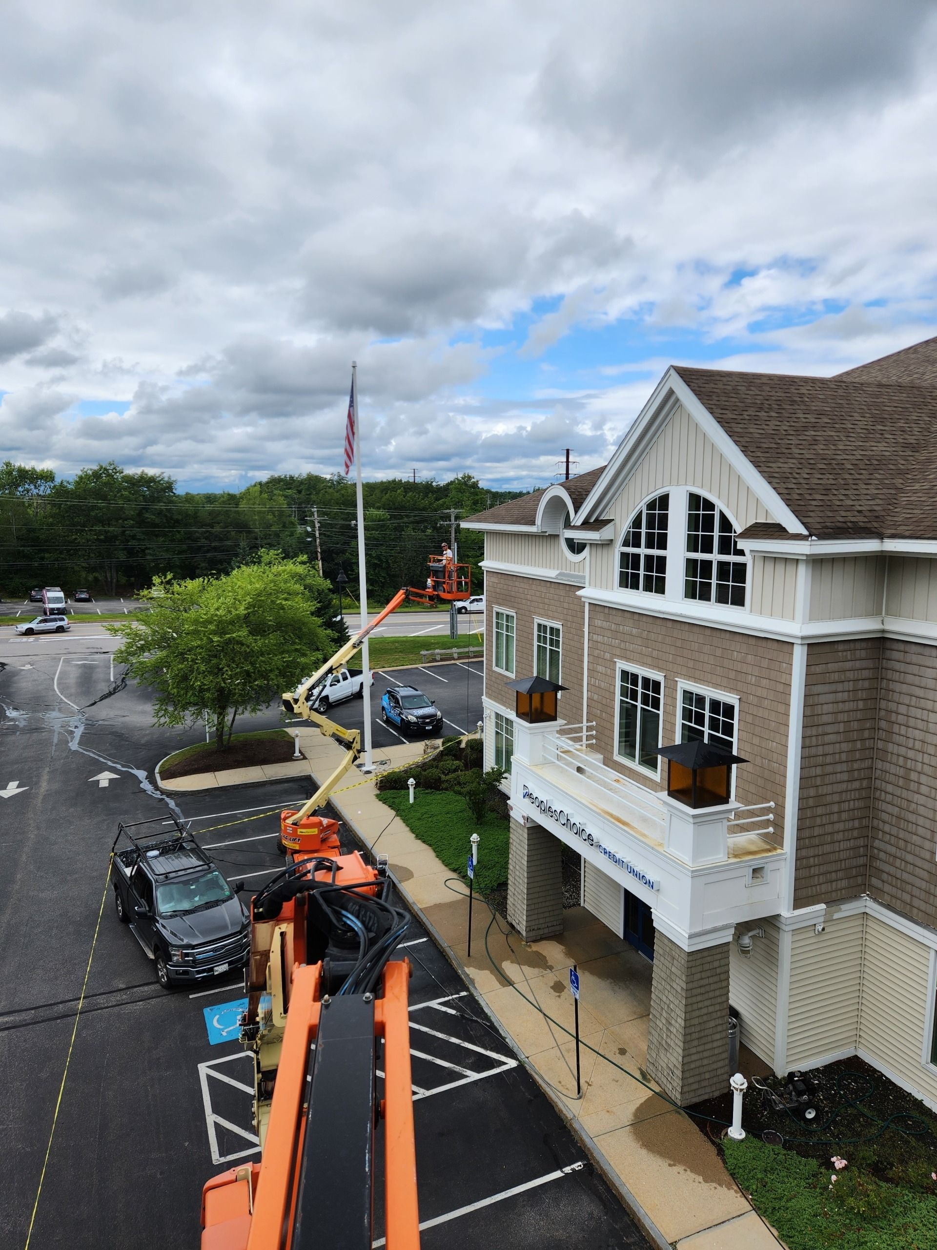 View of a building with a flagpole, overcast sky. Construction vehicle and cars in the parking lot.