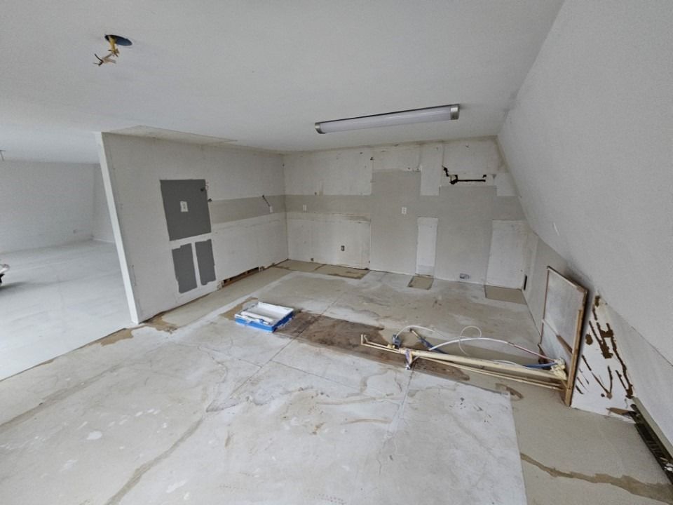 Room under construction: exposed walls, uneven floors, work materials scattered, overhead lighting.