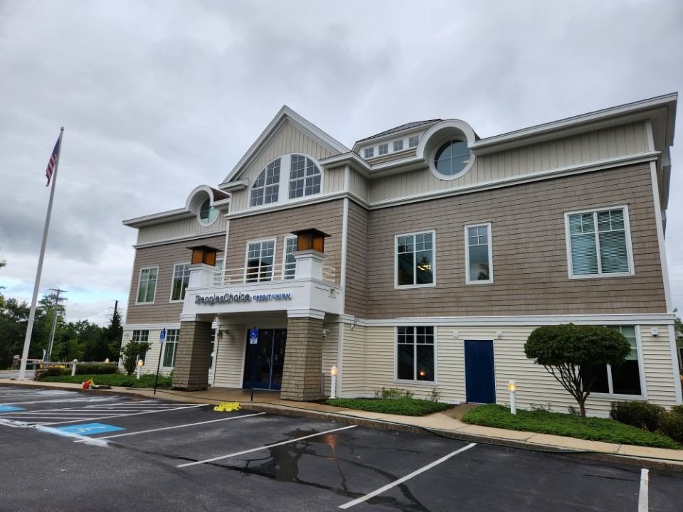 Two-story beige and brown building with blue doors and windows, cloudy sky, American flag.