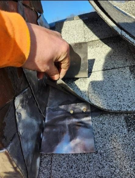 A hand placing flashing on a gray asphalt shingle roof.
