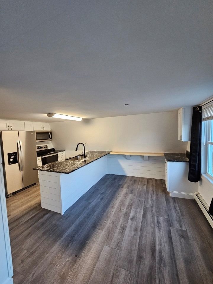 Modern kitchen with island, stainless steel appliances, and wood-look flooring. White cabinets, black countertops.
