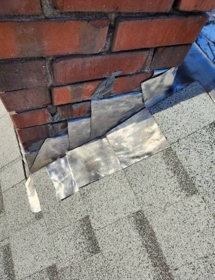 Brick chimney with gray roof shingles; flashing partially loose.