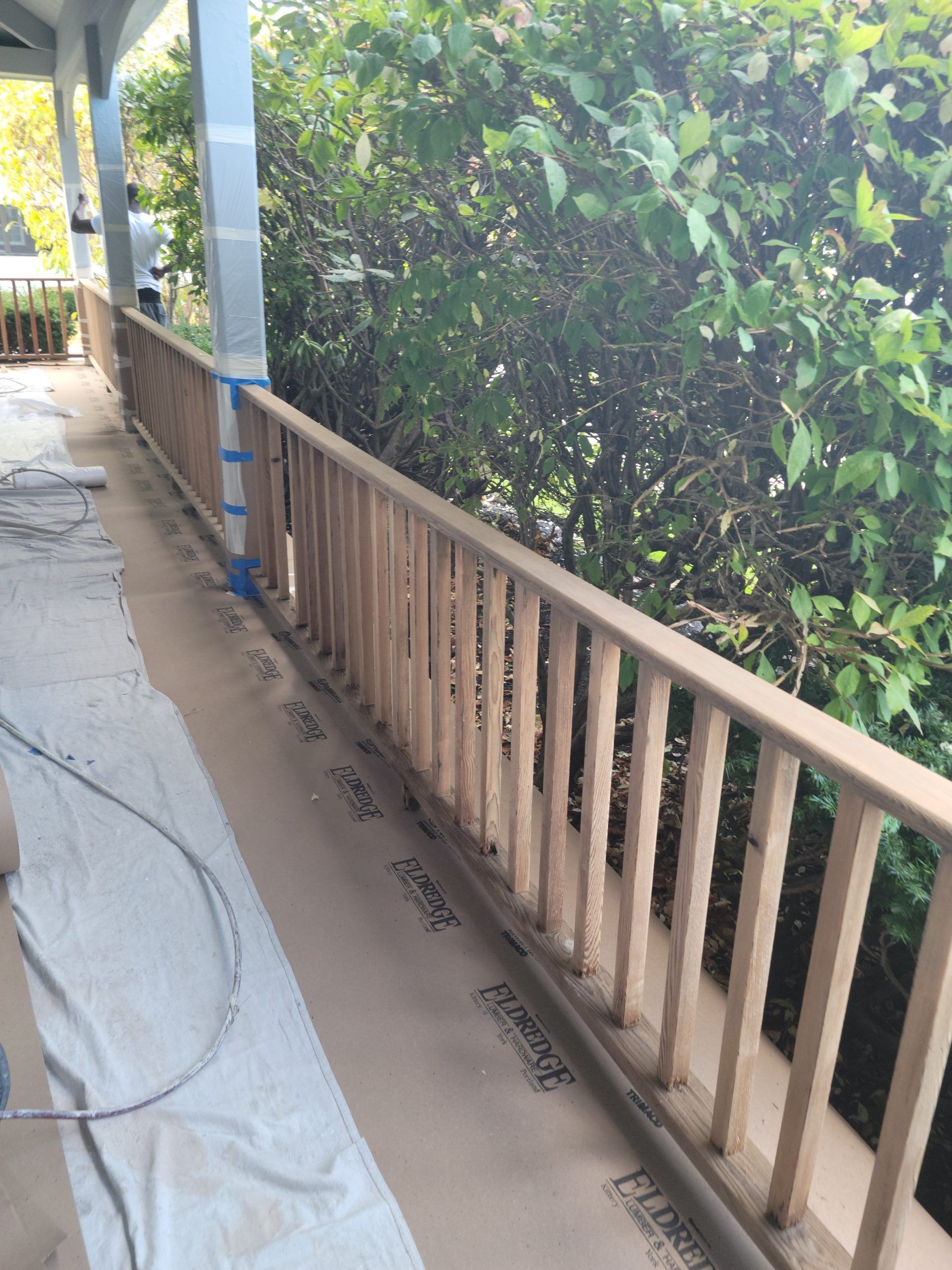A wooden railing on a porch, with a view of green foliage in the background.