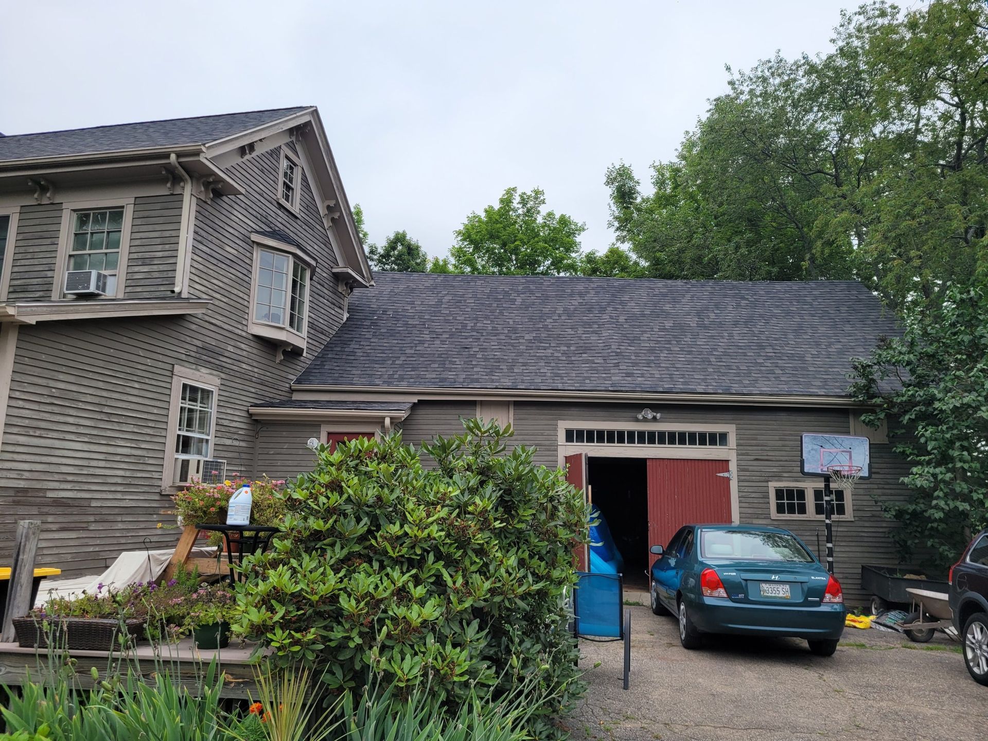 Gray house with attached garage, teal car in driveway, red garage door, overcast sky.