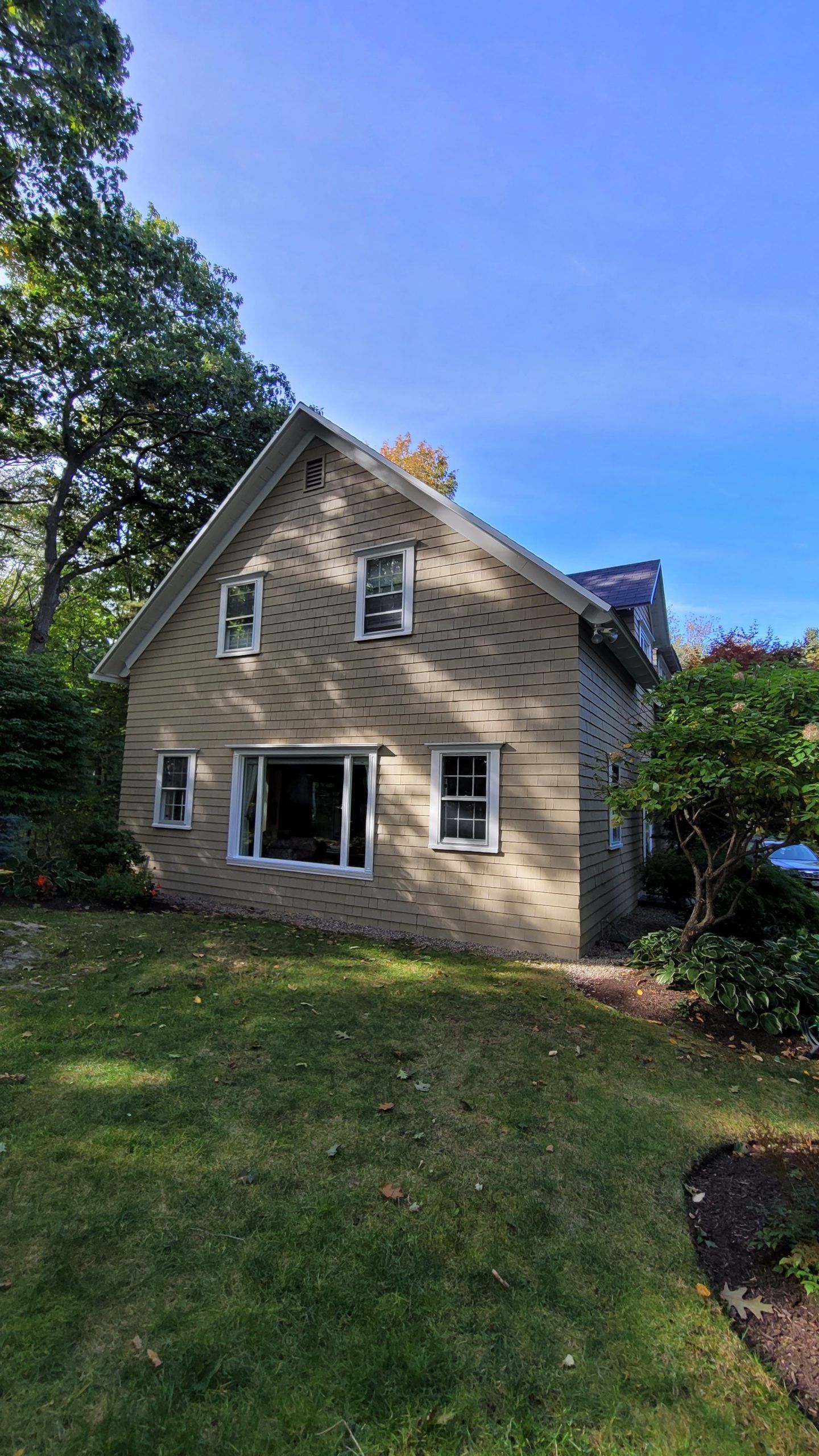 Tan brick house with multiple windows on a grassy lawn under a blue sky.