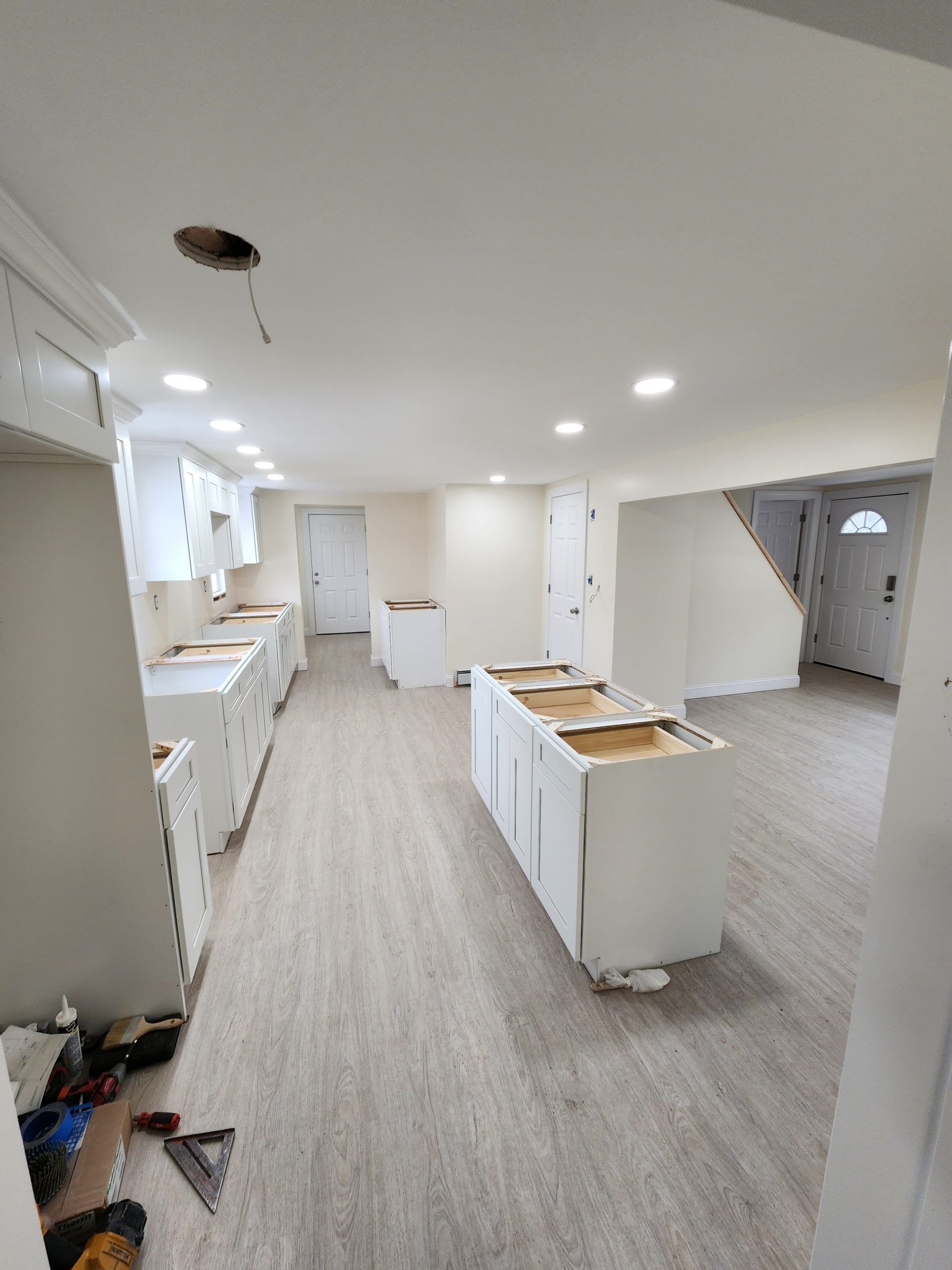 Unfinished kitchen with white cabinets and island. New flooring. Recessed lighting.