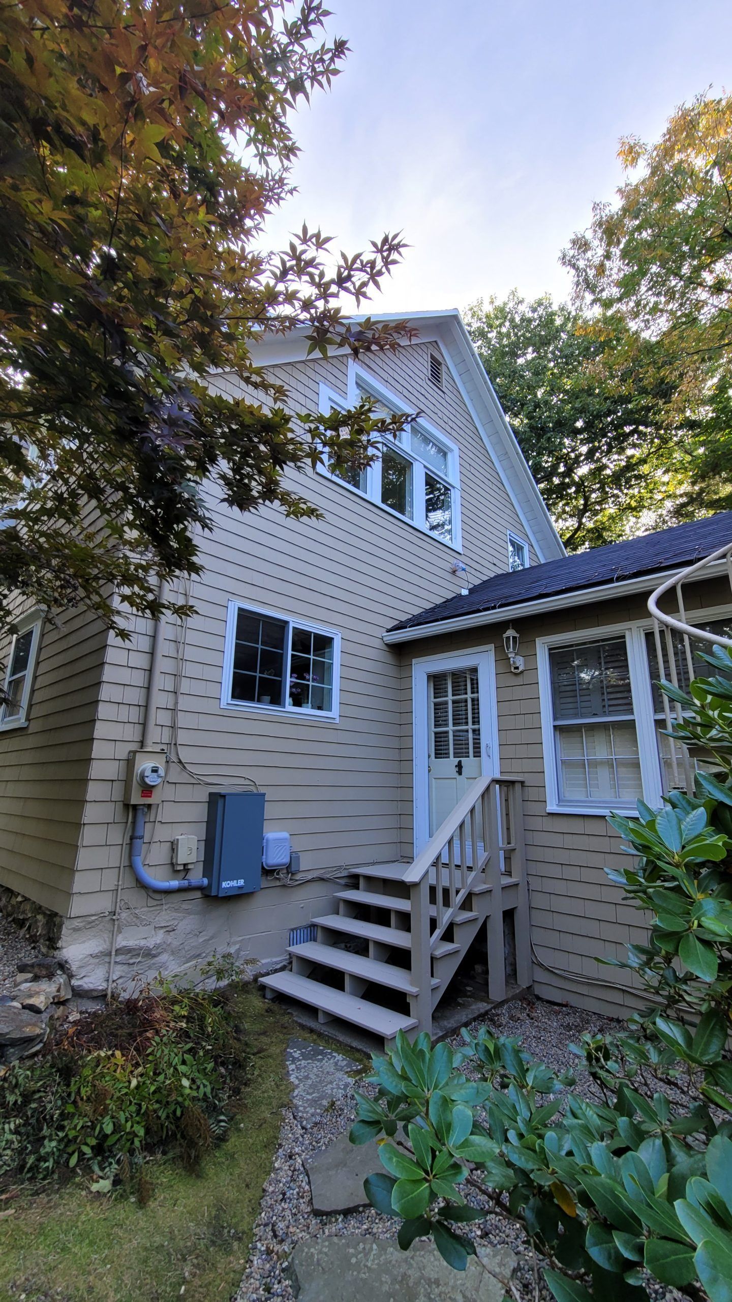Tan house with white trim, stairs, and a door surrounded by greenery.