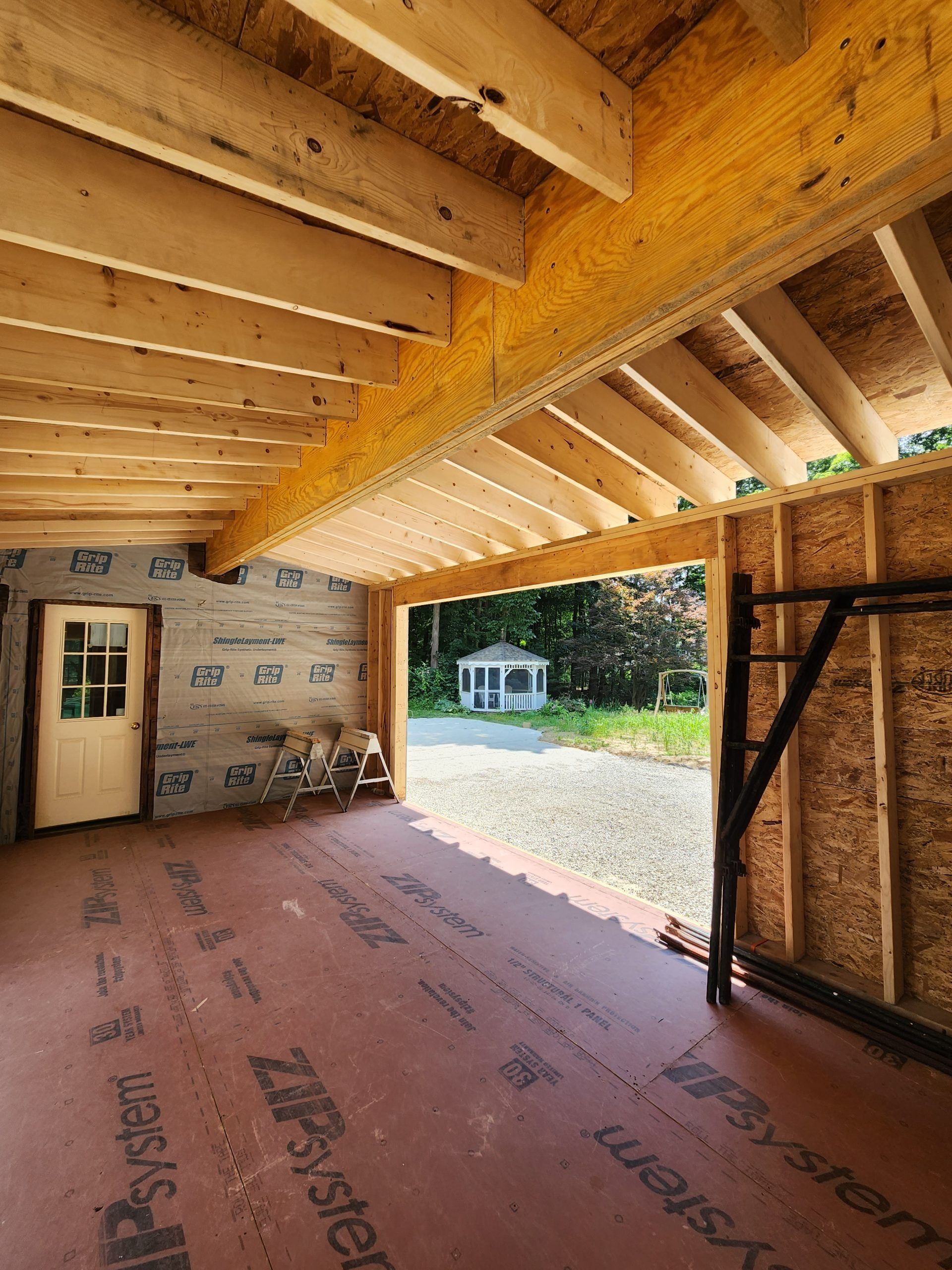 Open garage with wooden beams, framed walls, and exposed ceiling. Exterior view of a gazebo.