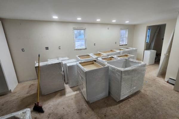 Kitchen renovation: cabinets wrapped in plastic are in a room with bare walls and windows.