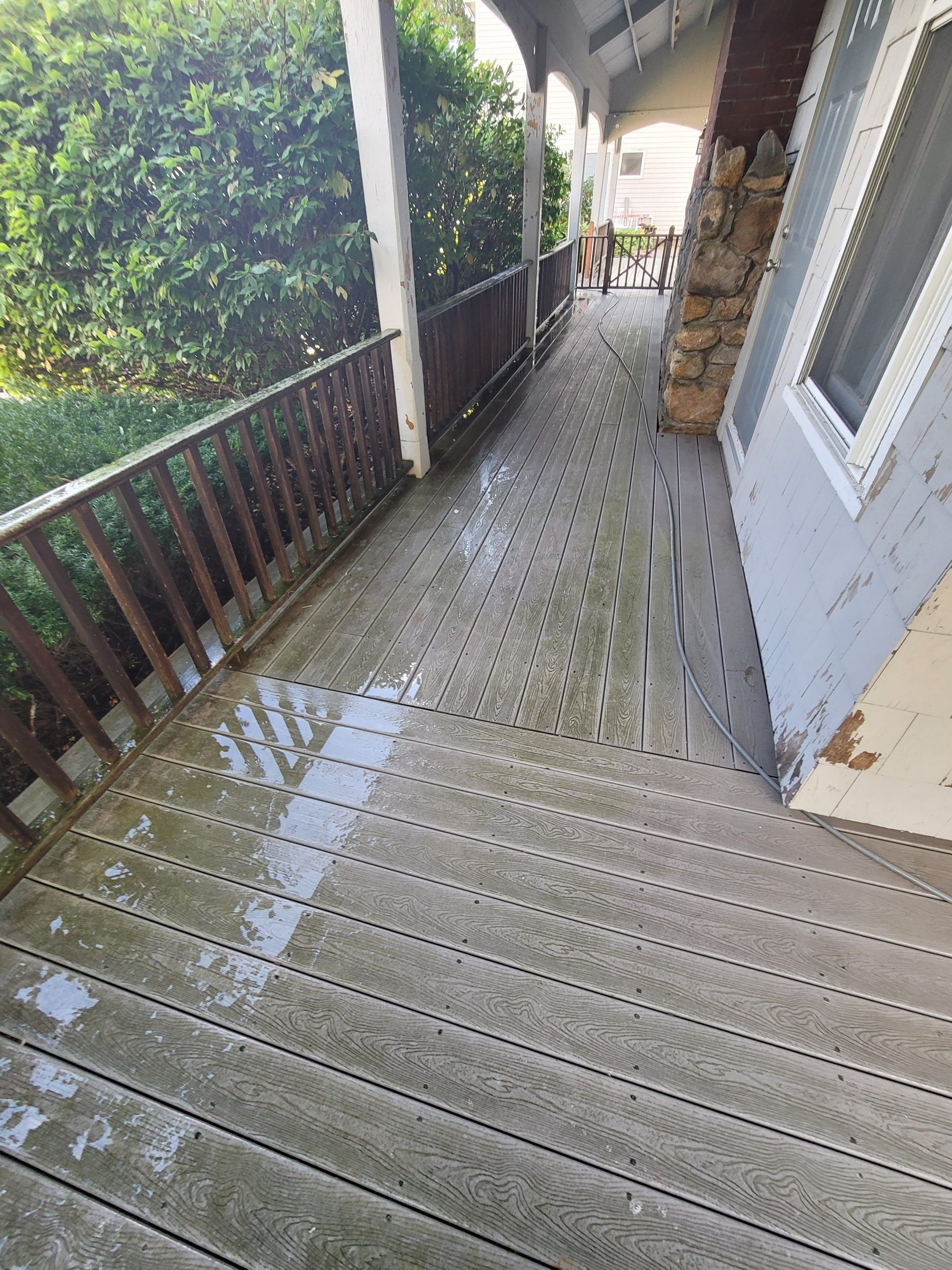 Wooden porch with wet surface and railing, alongside a house with a stone and wood facade.
