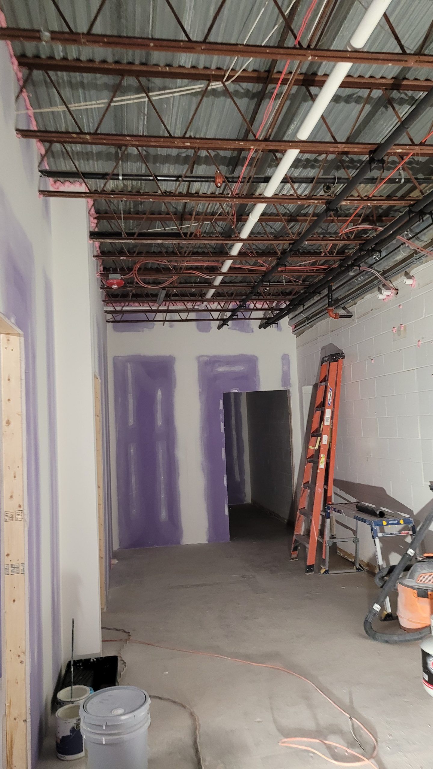 Interior view of a construction site. Walls are purple drywall, with exposed beams and wiring on the ceiling.