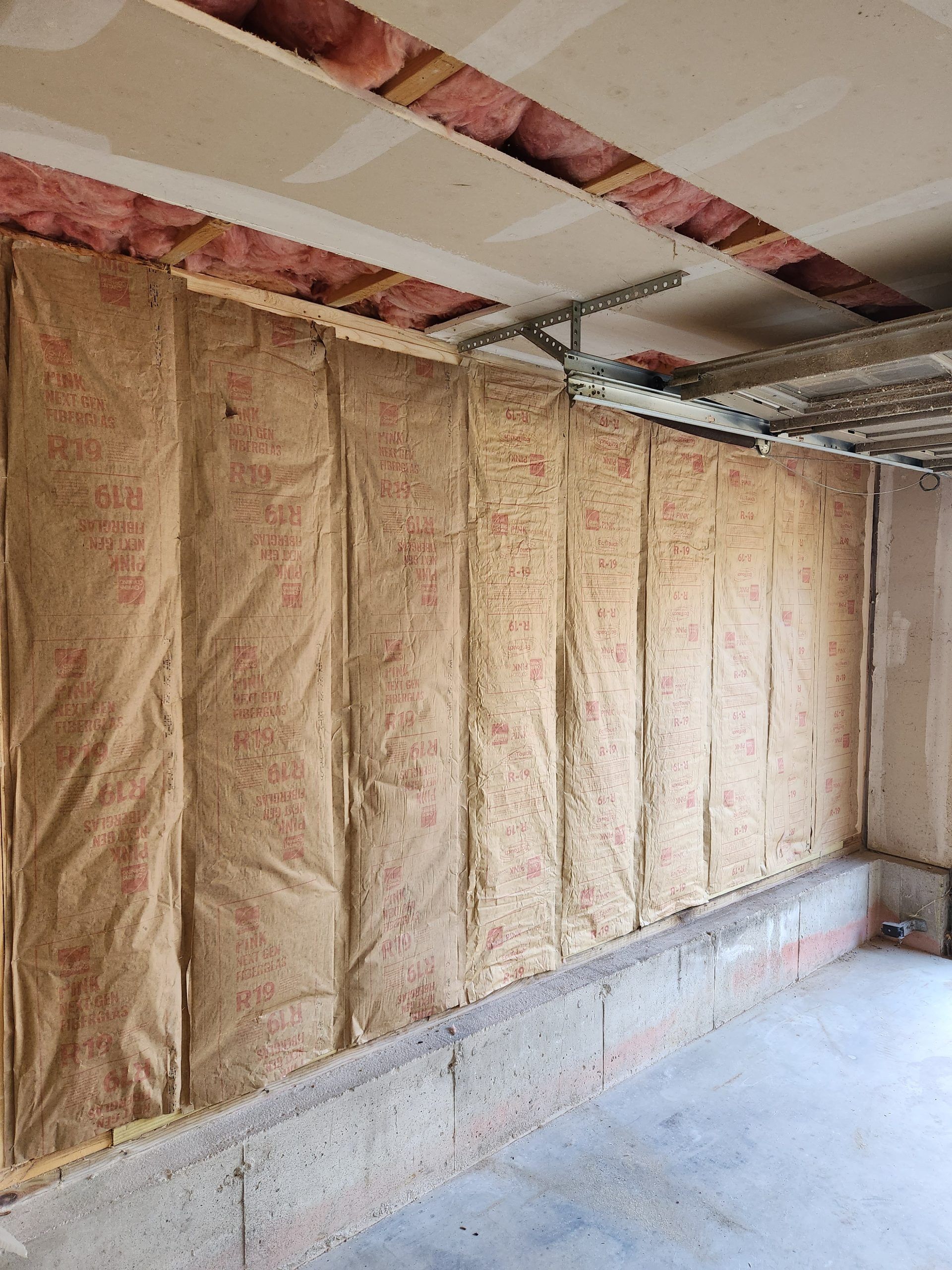 Garage wall with insulation installed, ready for drywall. Beige insulation between studs.