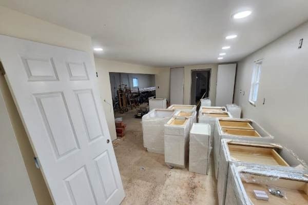 Kitchen renovation in progress, white cabinets ready for installation, open space, overhead lighting, door.