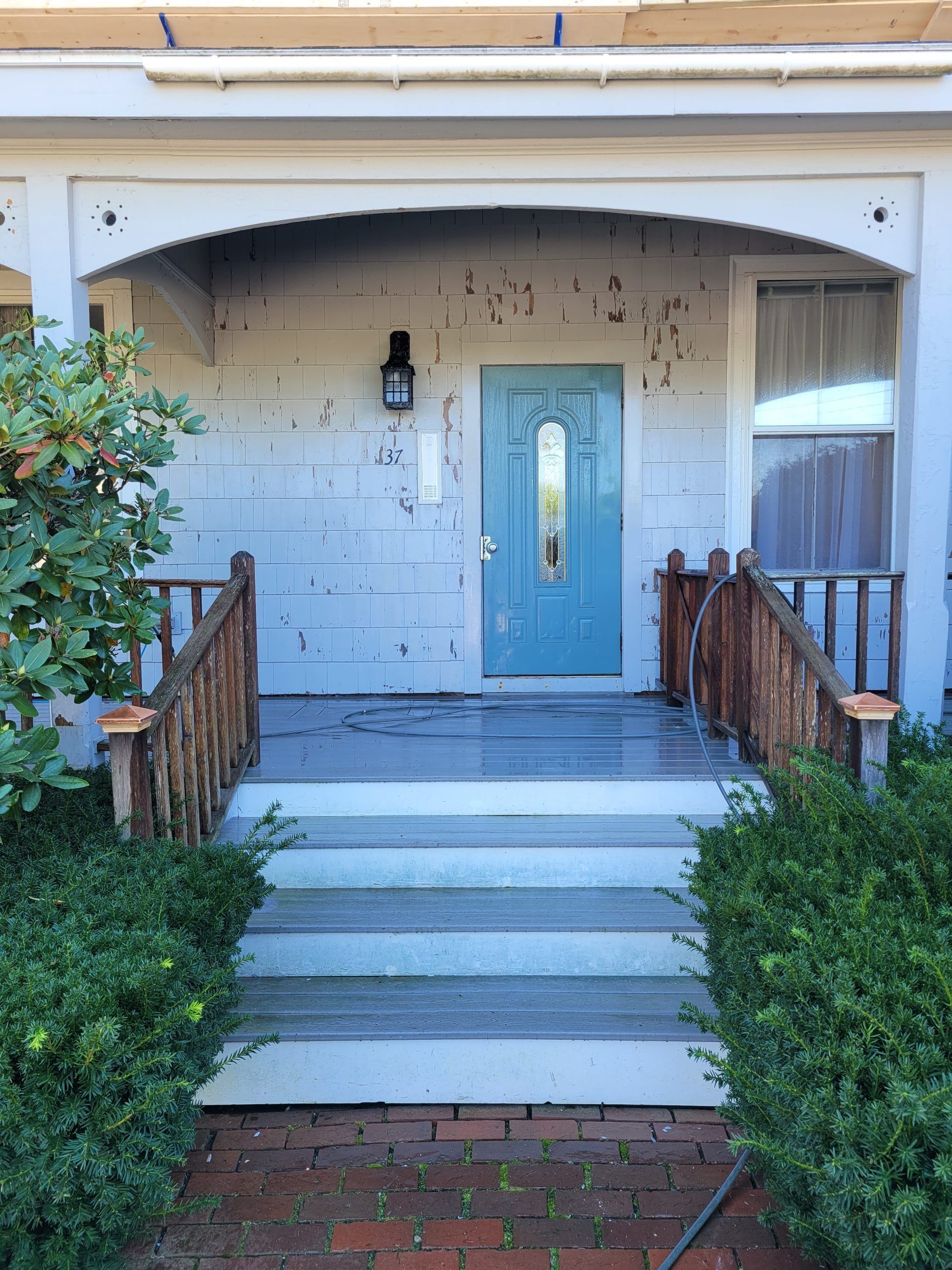 Front porch with steps leading to a blue door under an arched portico. Weathered wood and peeling paint.