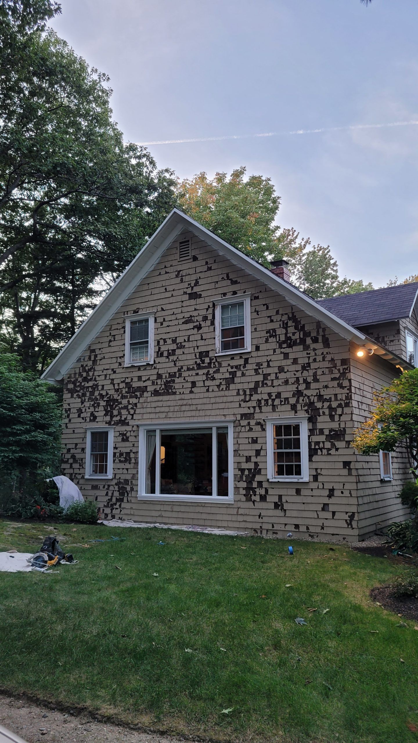 Beige house with peeling paint, windows, and a green lawn.