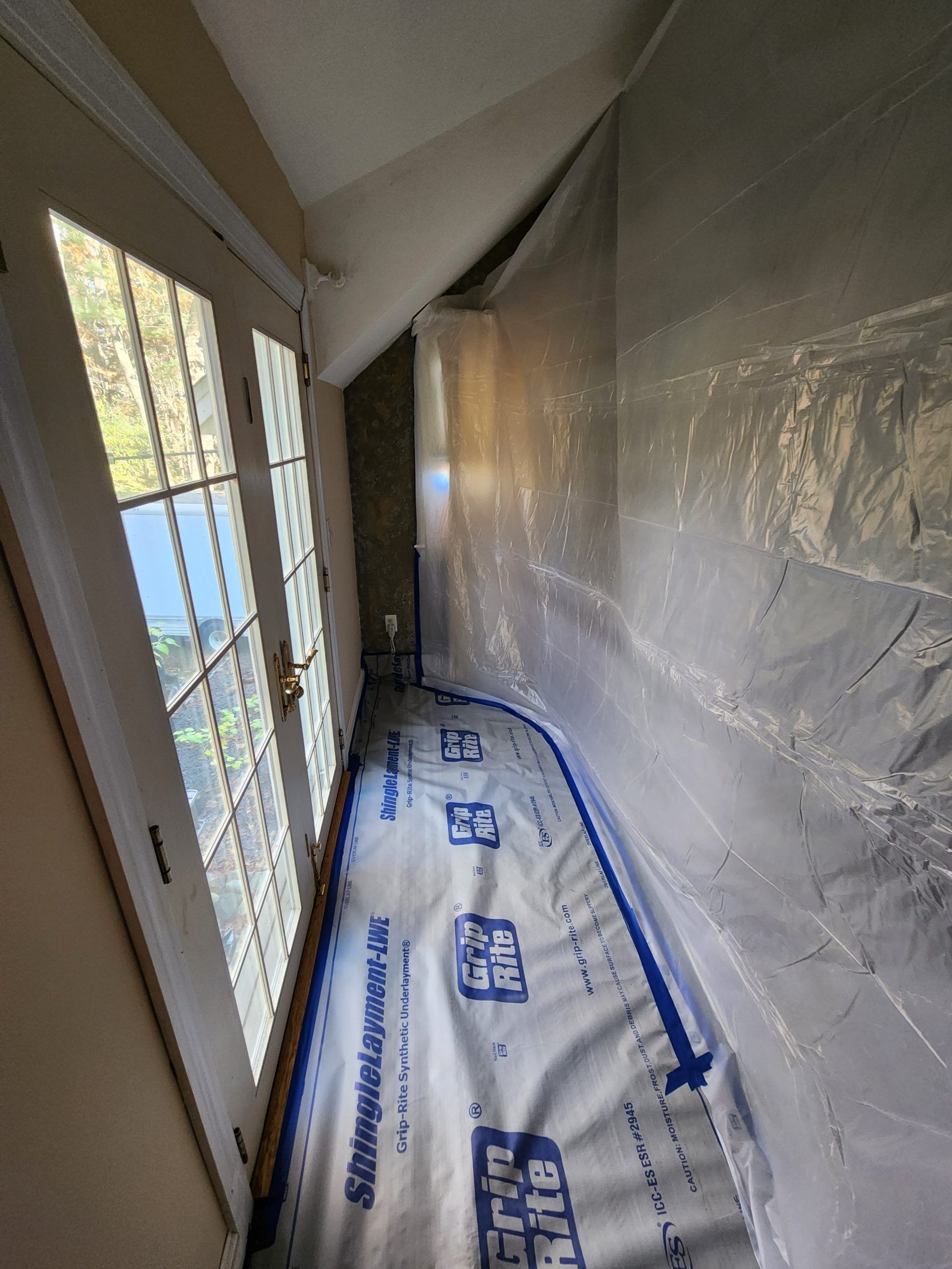 Interior hallway with plastic sheeting and floor protection. French doors to the left.