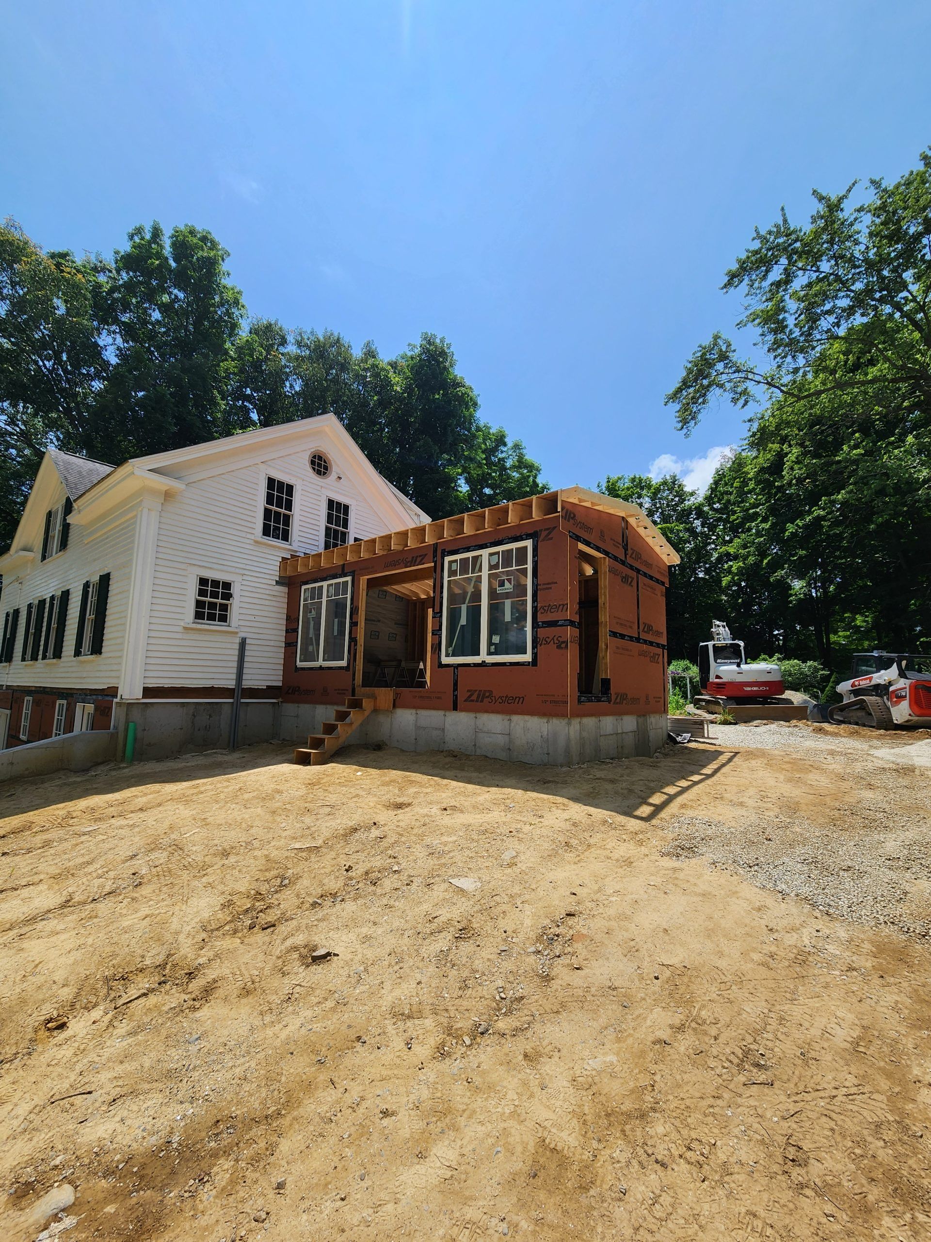 House under construction, addition being built with wood framing, windows installed, sunny day.