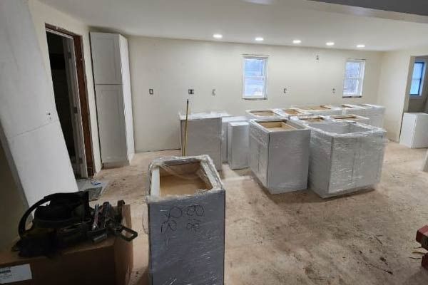 Kitchen renovation: unfinished cabinets wrapped in plastic on a dusty floor, walls are bare.