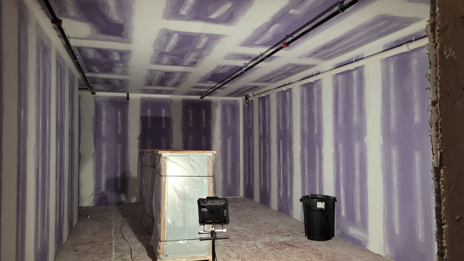 Interior construction view with purple drywall, black pipes, and construction materials.