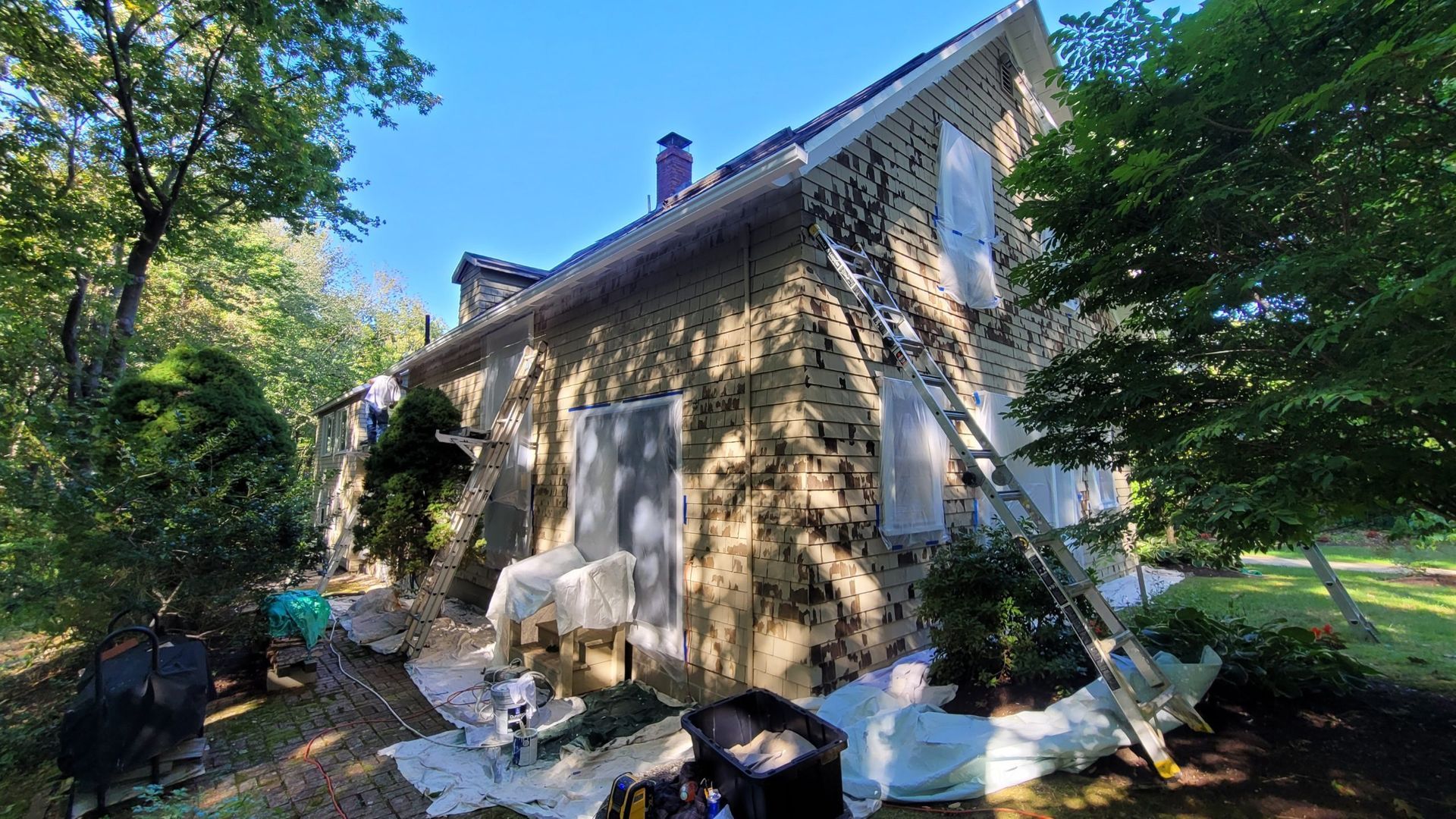 House exterior with ladders and painting supplies; siding being renovated on a sunny day.