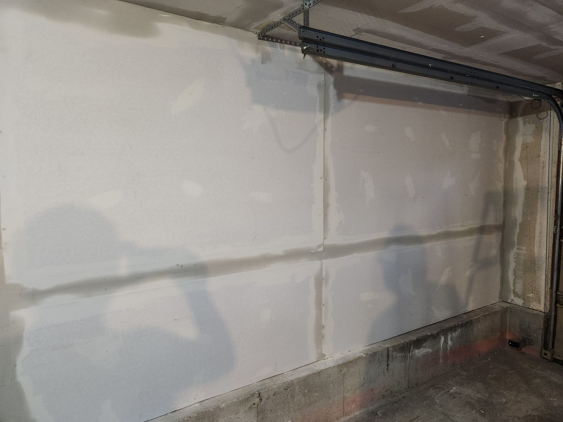 White drywall on a concrete wall, seams visible, pipes above.