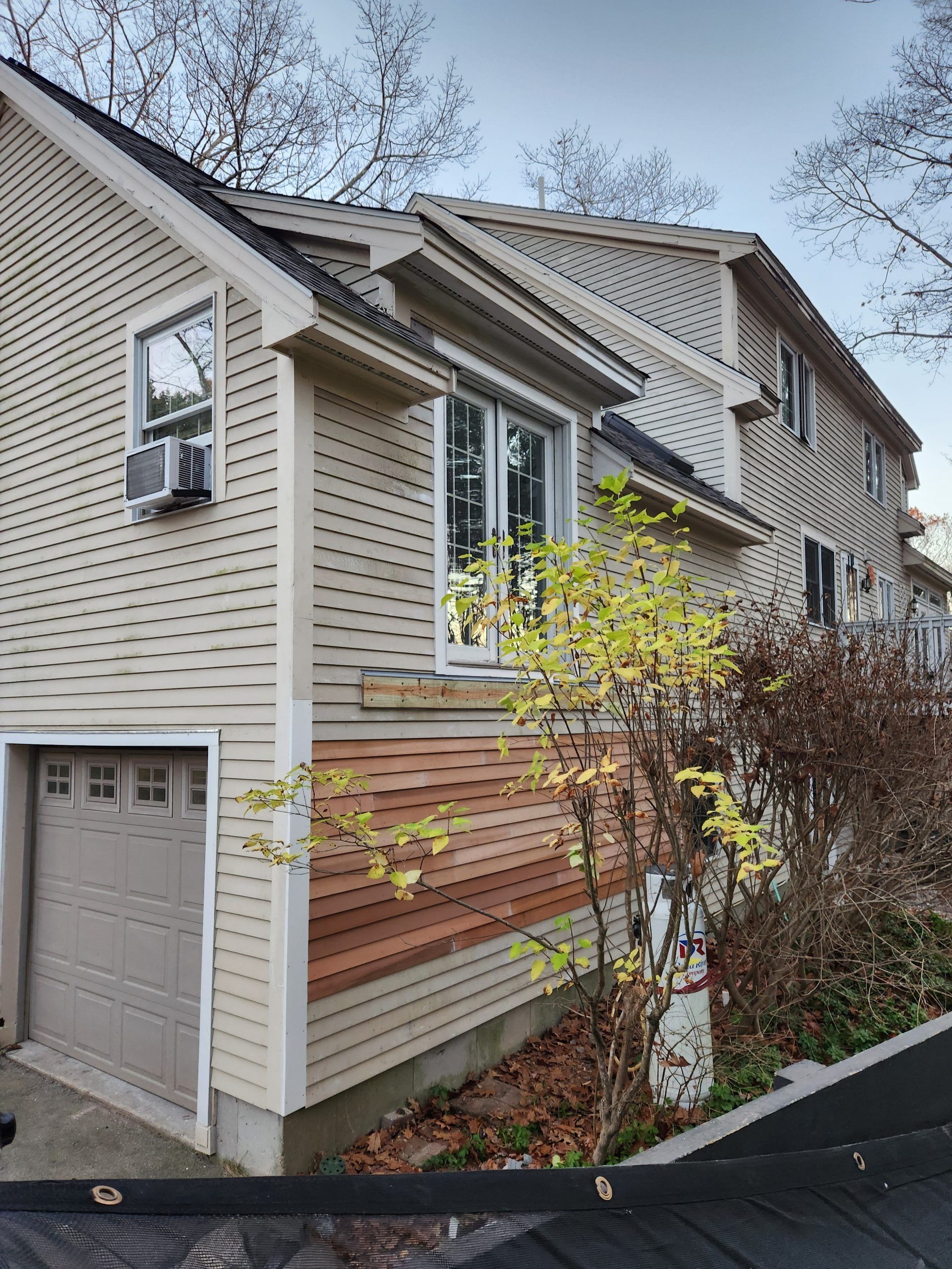 Beige house with a garage and two stories, tan siding, brown wood paneling, and an air conditioner in the window.