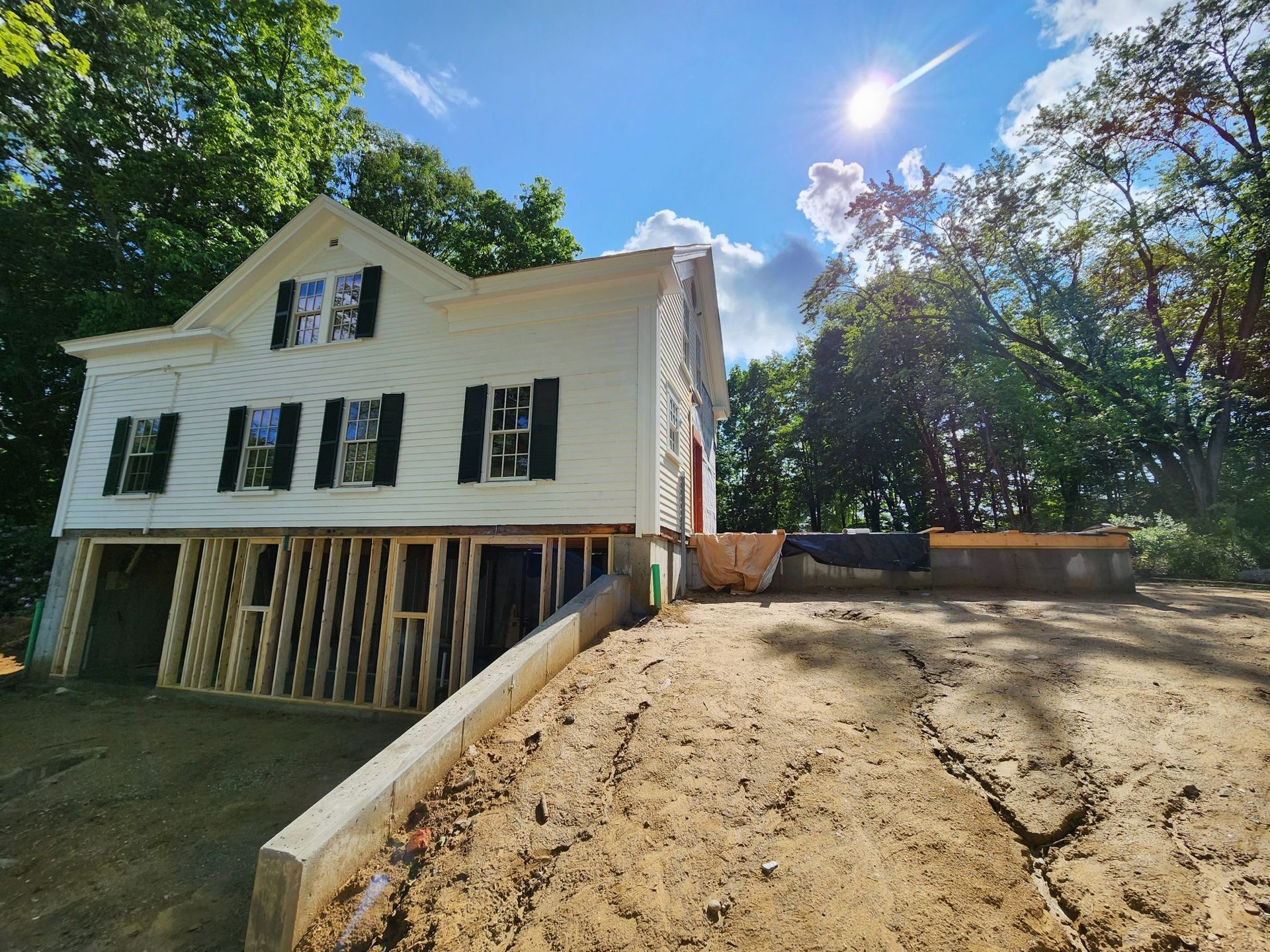 White house under construction, supported by wooden beams, dirt lot in the foreground, sunny day.