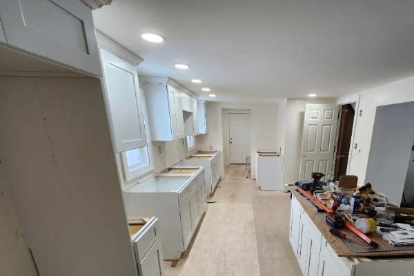 Kitchen with white cabinets under construction, some upper cabinets installed. Tools on island.