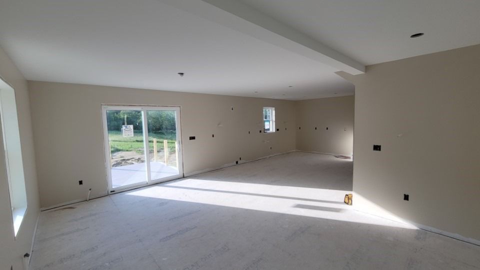 Empty room with light beige walls and white ceiling; large sliding glass door and windows let in natural light.
