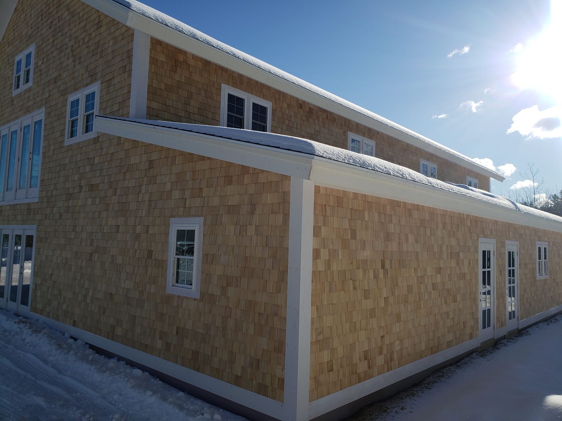 Two-story building with light brown cedar shake siding, white trim, and snow on the roof.