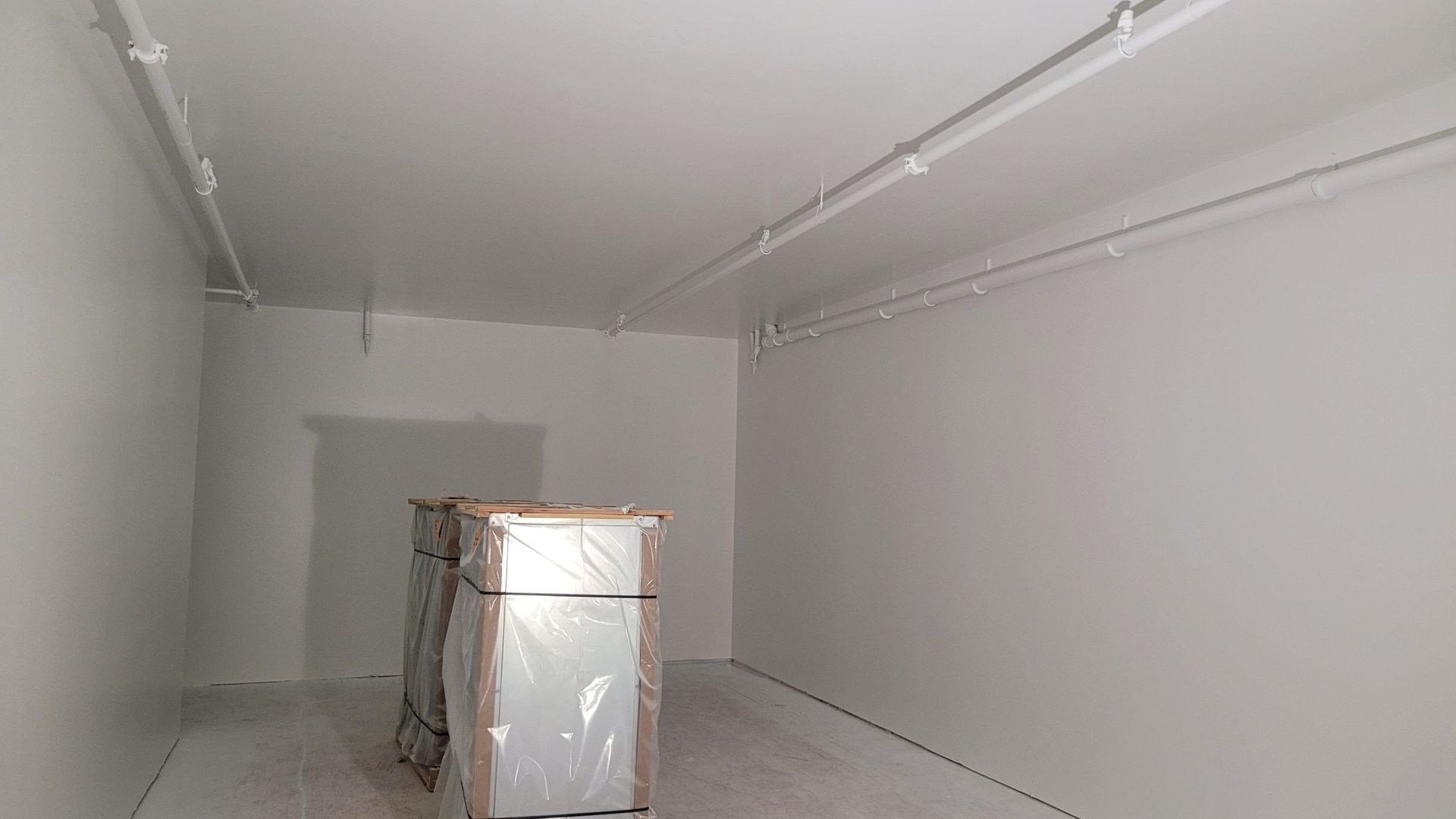 Empty white room with conduit lighting, and packaged items near a doorway.