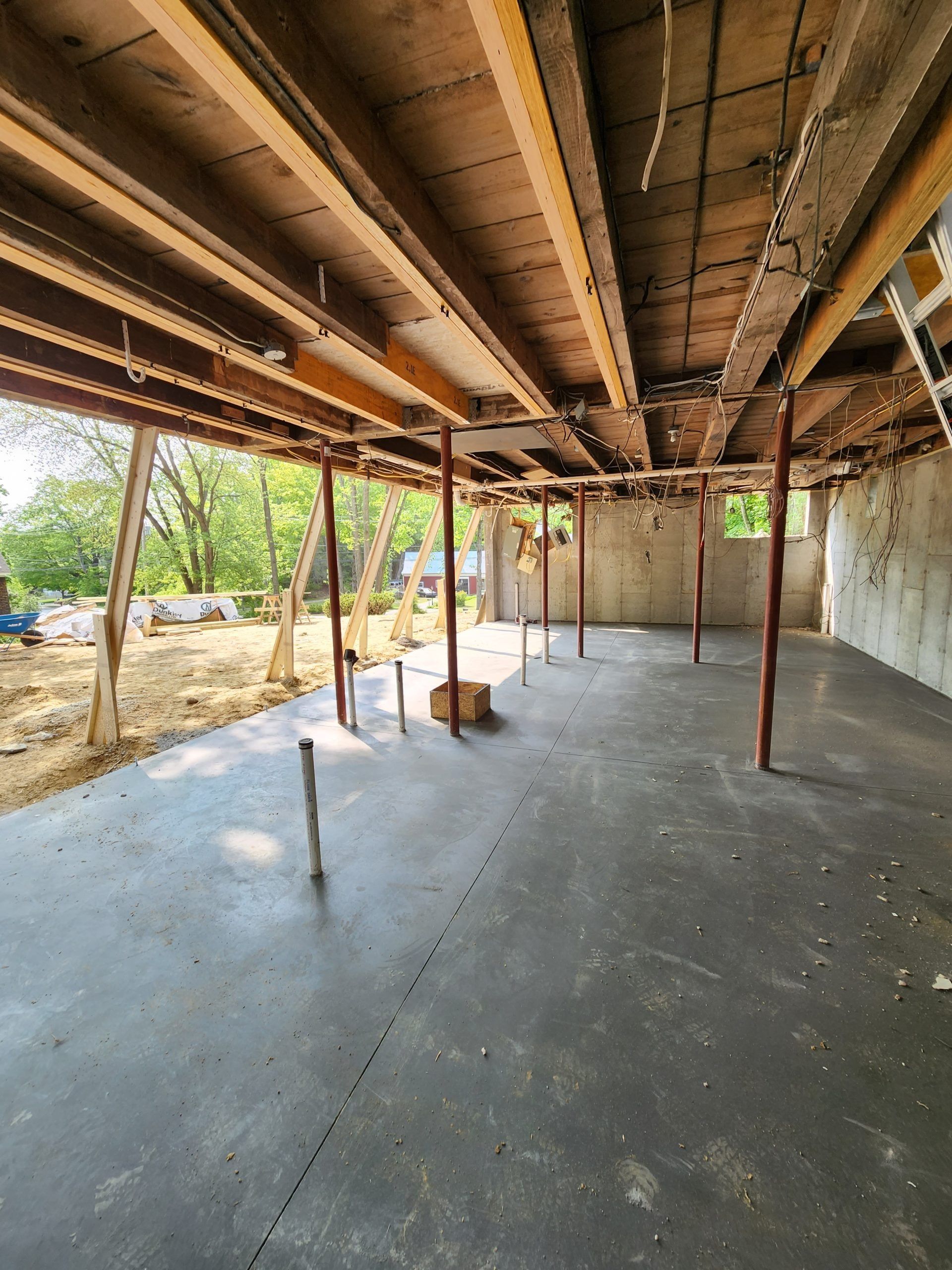 Concrete-floored basement under construction, supported by columns and beams. Visible unfinished walls and plumbing.