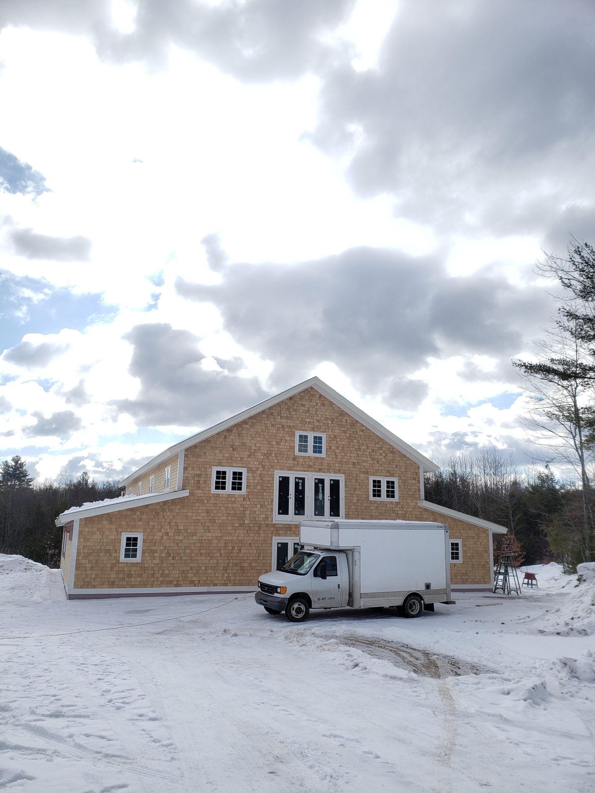 New house under construction, with wooden siding, white windows, and a white delivery truck parked in the snow.