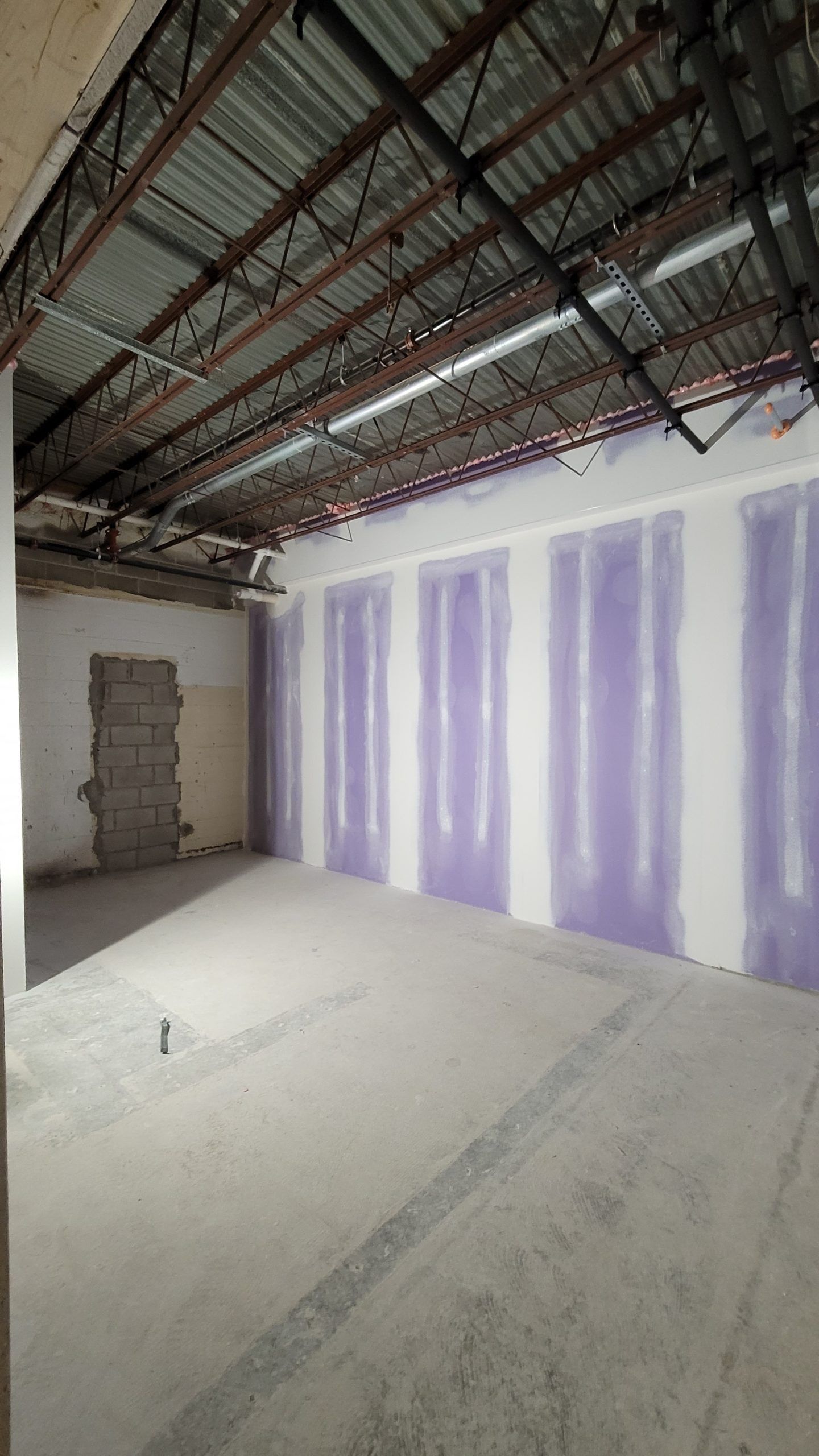 Interior of a room under construction, with exposed metal ceiling, drywall and concrete floor.