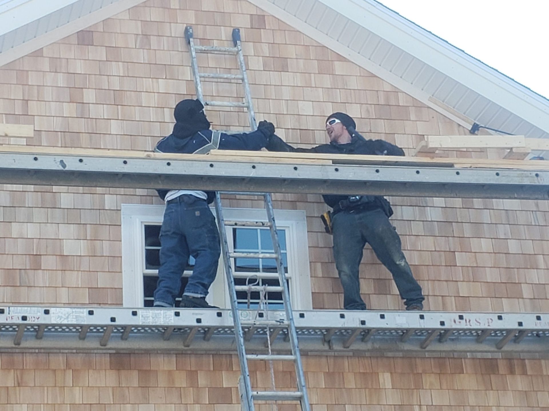 Three workers on scaffolding near a building, installing cedar shingles.