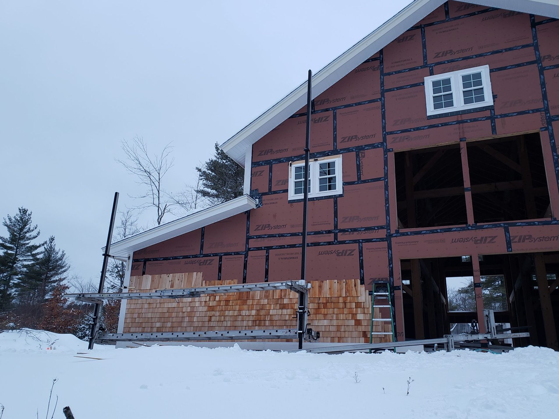 Building exterior under construction; brown siding, white windows, snow-covered ground, scaffolding.