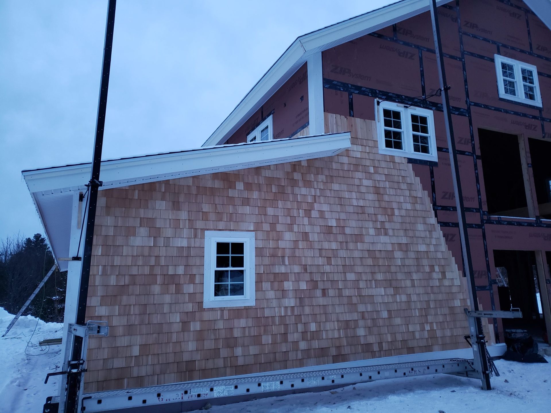 New house construction with cedar shingle siding and snow on the ground.