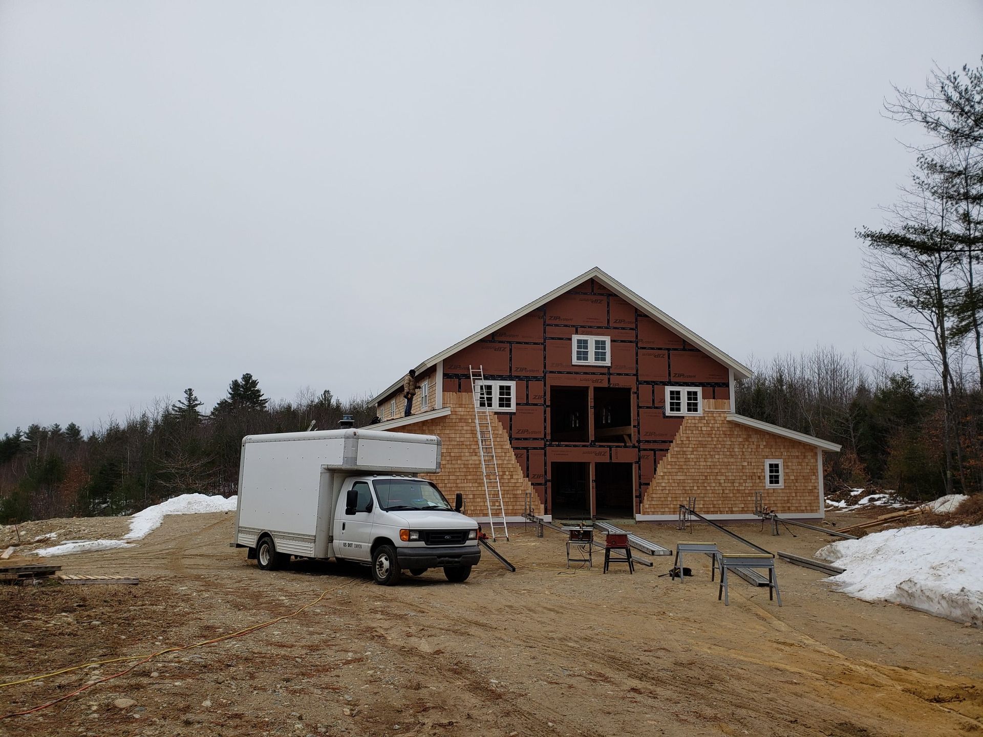 White delivery truck parked in front of a partially constructed two-story building on a dirt lot.