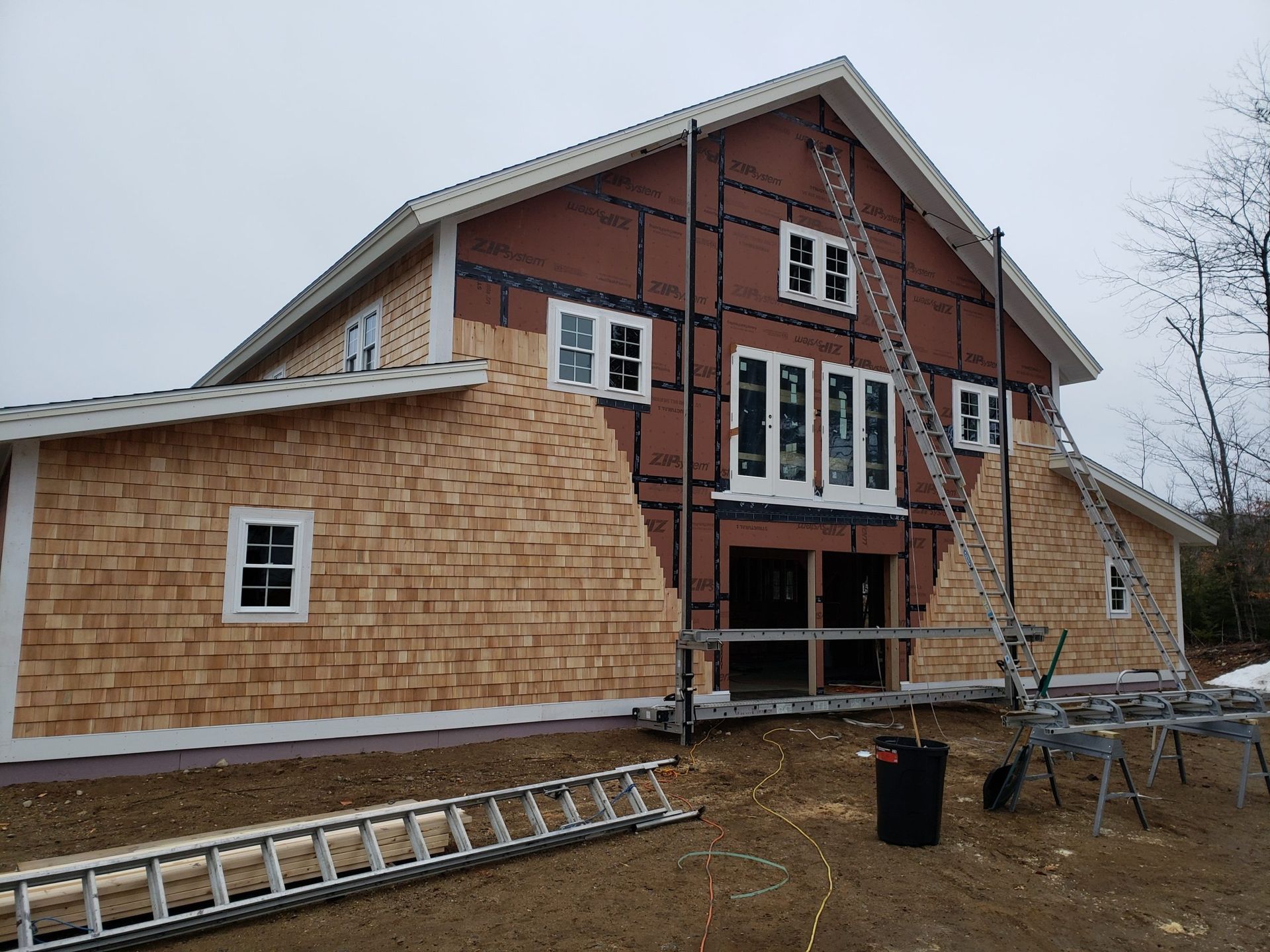 Construction of a two-story building with wood shingle siding and brown siding. Ladders and materials are present.