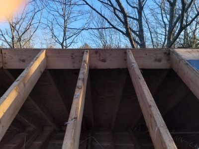 Wooden rafters and beams against a blue sky, likely a building under construction.