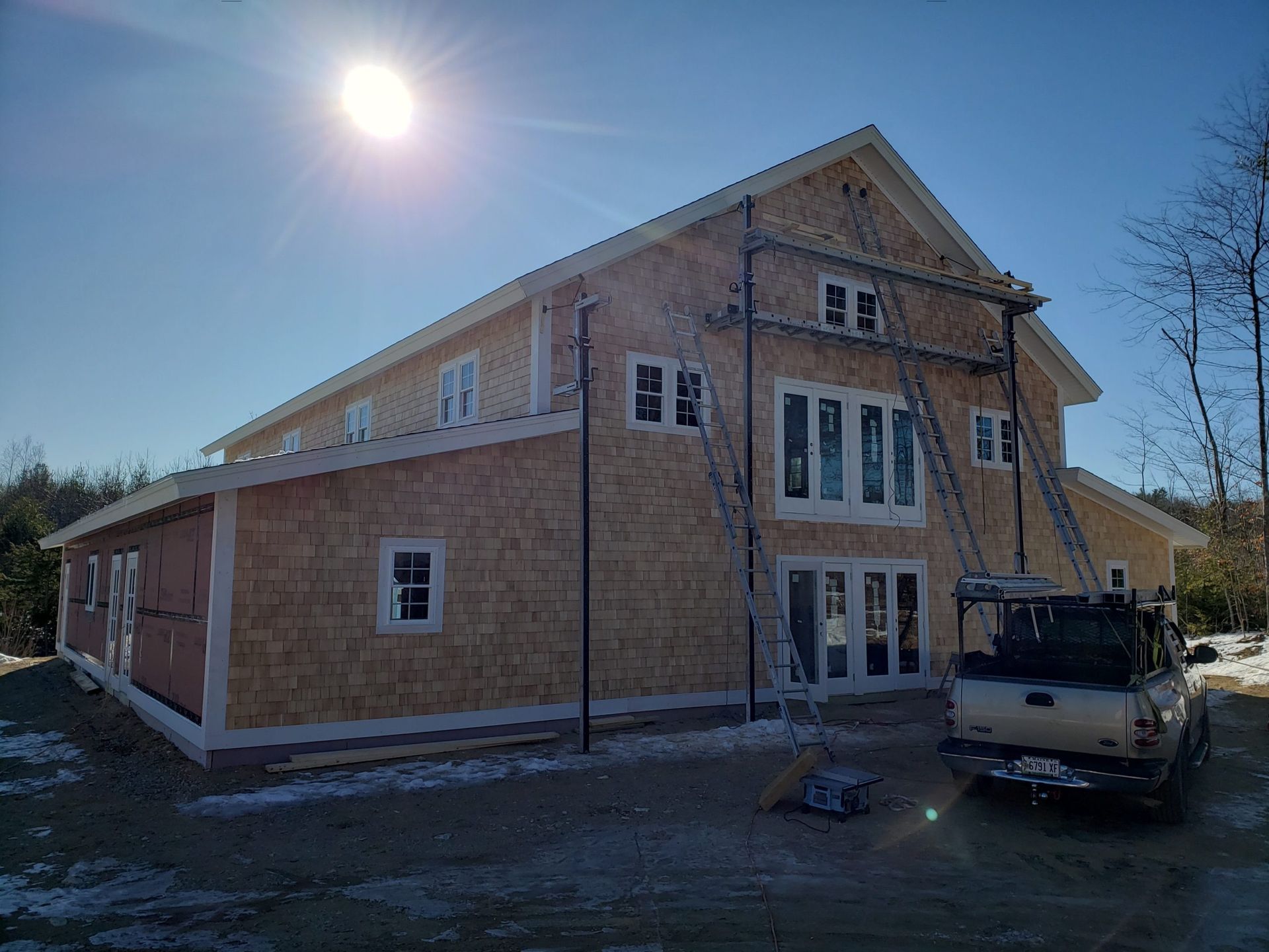 House under construction; wood siding, scaffolding, sunny day.