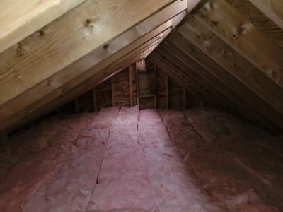 Attic interior with pink insulation on the floor, wooden beams overhead.