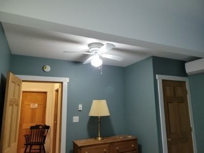 A room with a ceiling fan, dresser, lamp, and doors. Teal walls, white trim.