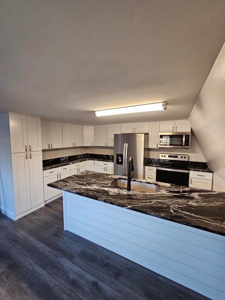 White kitchen with dark countertops and island, stainless steel appliances, and gray flooring.
