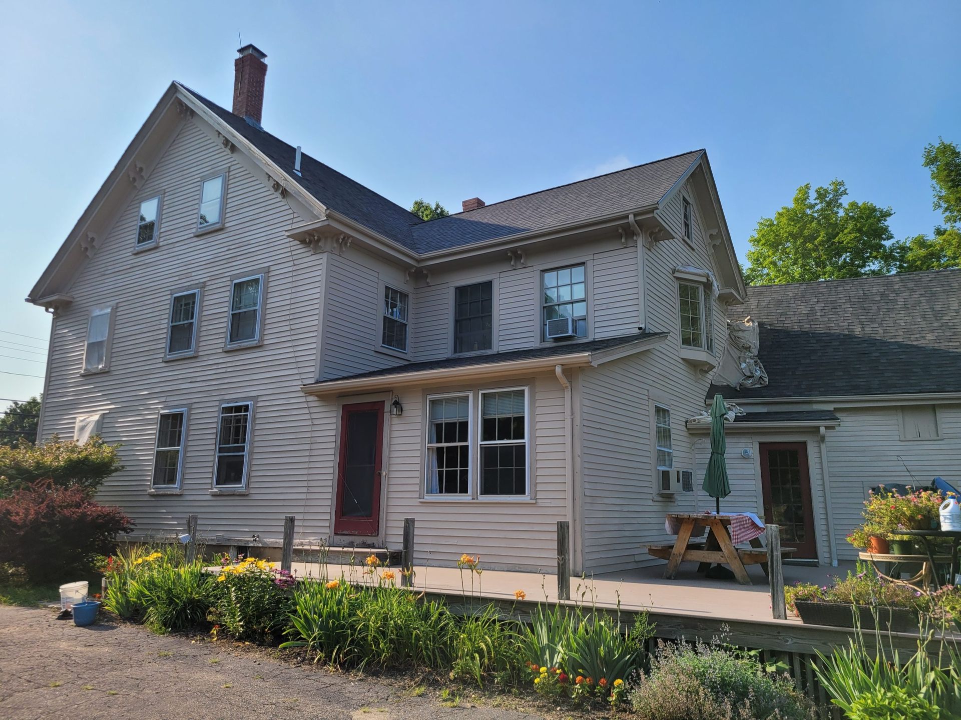 Two-story house with a red door, a dark roof, and a flower garden in front.