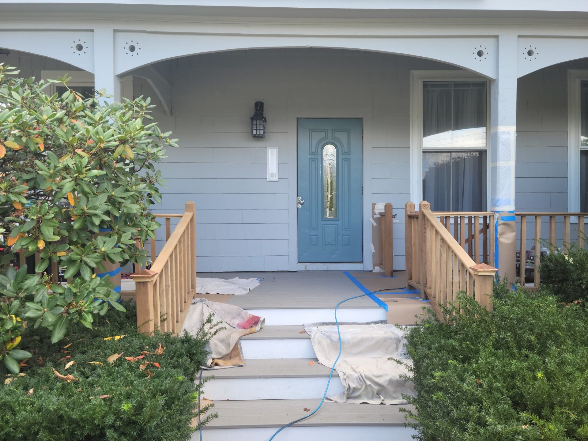 A blue front door and porch with wooden railings, steps, and gray siding.