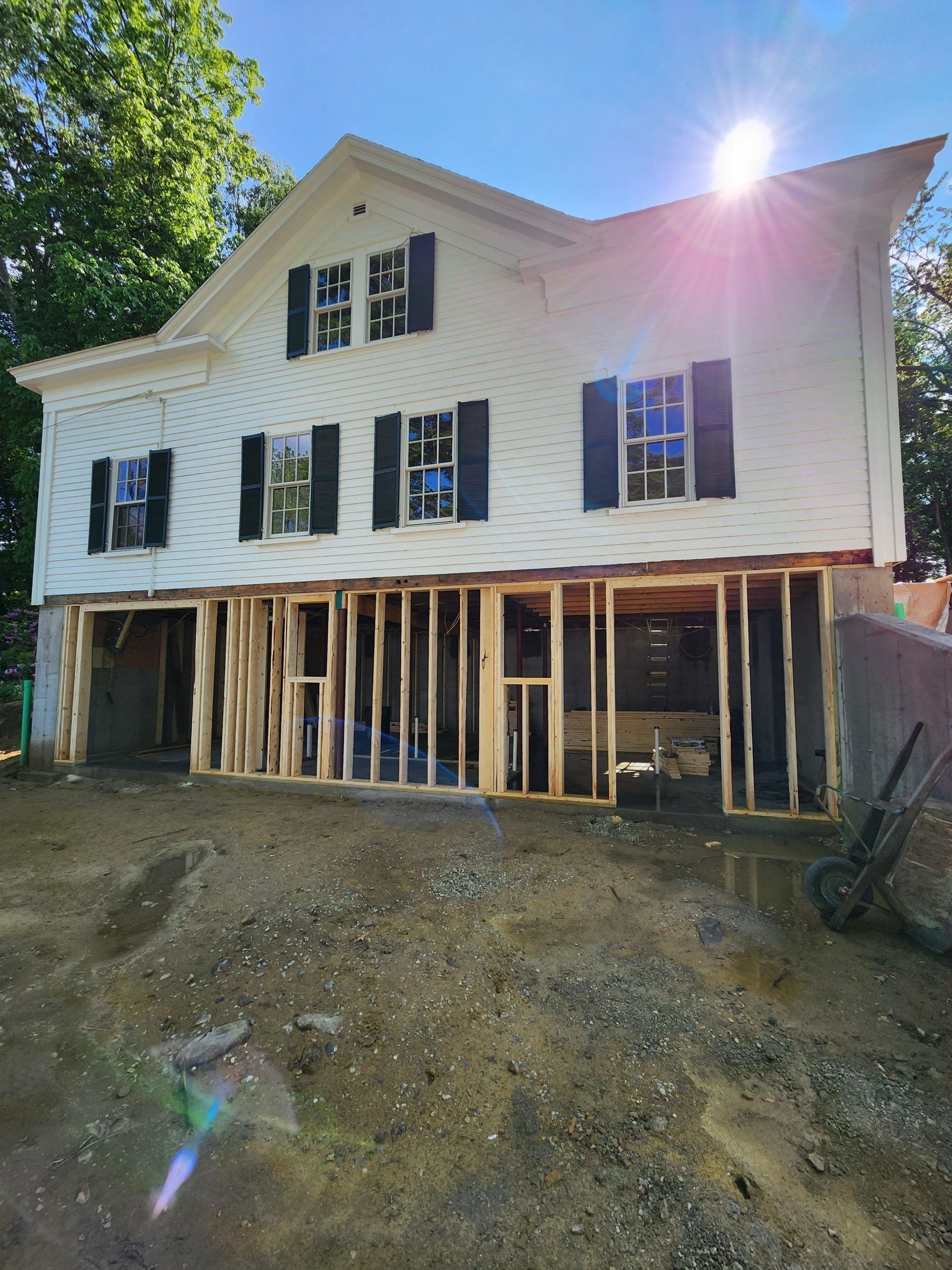 Two-story white house under construction, exposed wooden framing on ground level, sunny day.